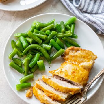 white plate with chicken and green beans on it. fork next to chicken. striped towel next to plates.