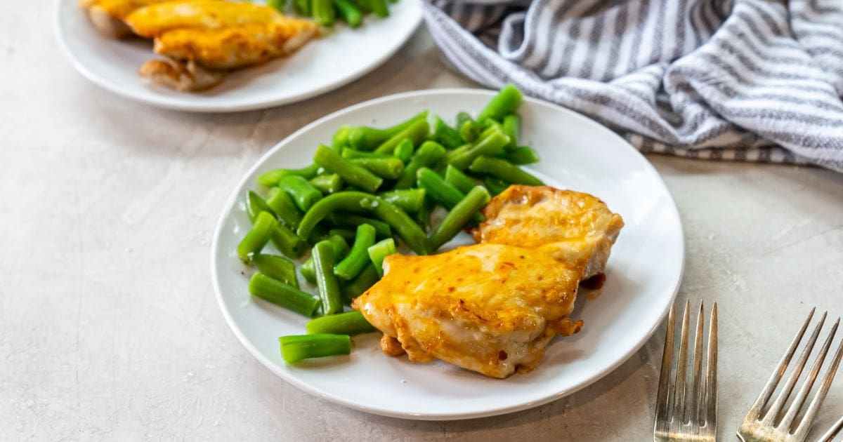 white plate with chicken and green beans on it. fork next to chicken. striped towel next to plates.