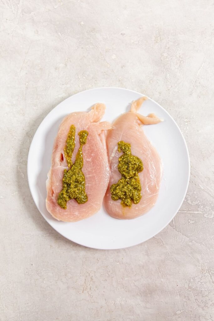 Air Fryer Pesto Chicken Breast white plate with raw chicken and pesto spreader all over the chicken breast