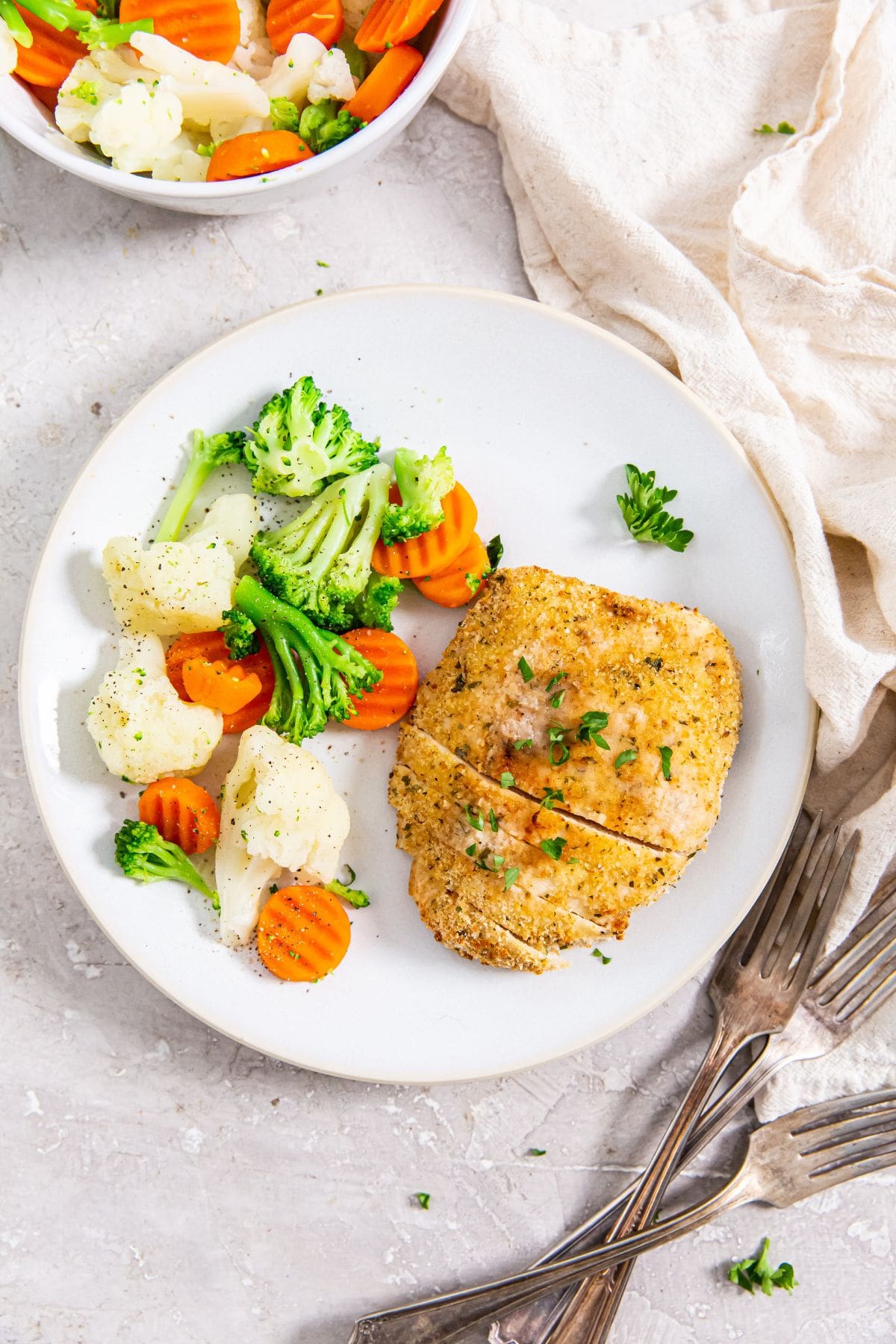 Air Fryer Chicken Cutlets white plate with chicken and vegetables. Silverware and towels next to it.