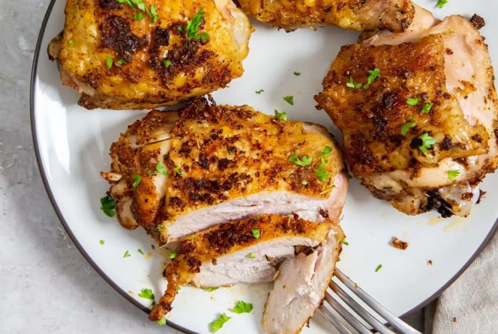 Air Fryer chicken thighs on a white plate, garnished with chopped parsley, one thigh sliced to show juicy interior.