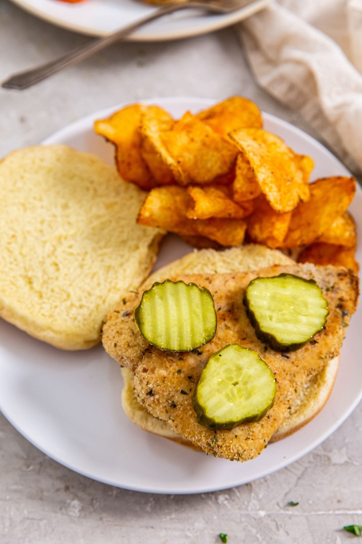 Air Fryer Chicken Cutlets white plate with chicken sandwich and chips on it.