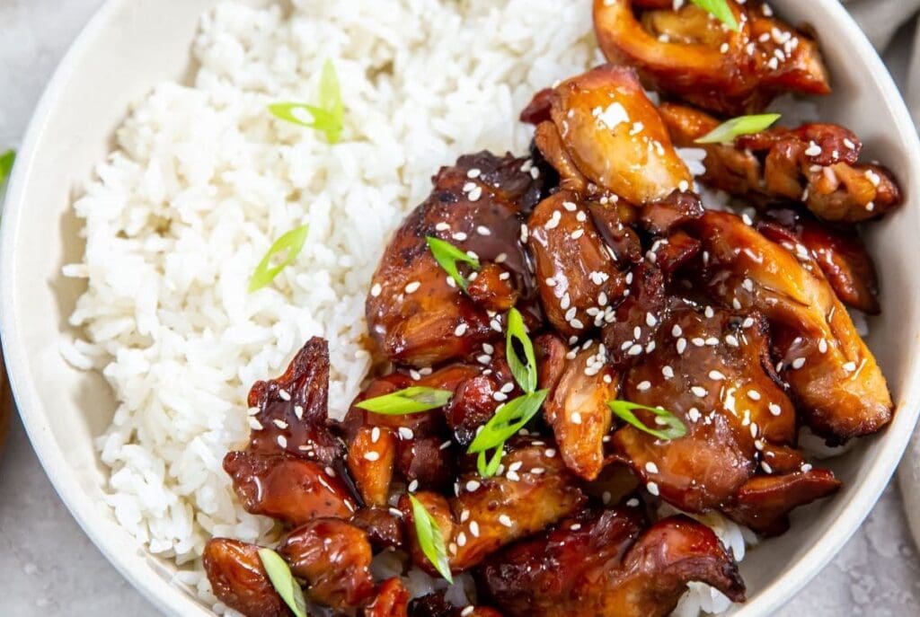 Bowl of air fryer teriyaki chicken with sesame seeds and green onions, served alongside white rice.