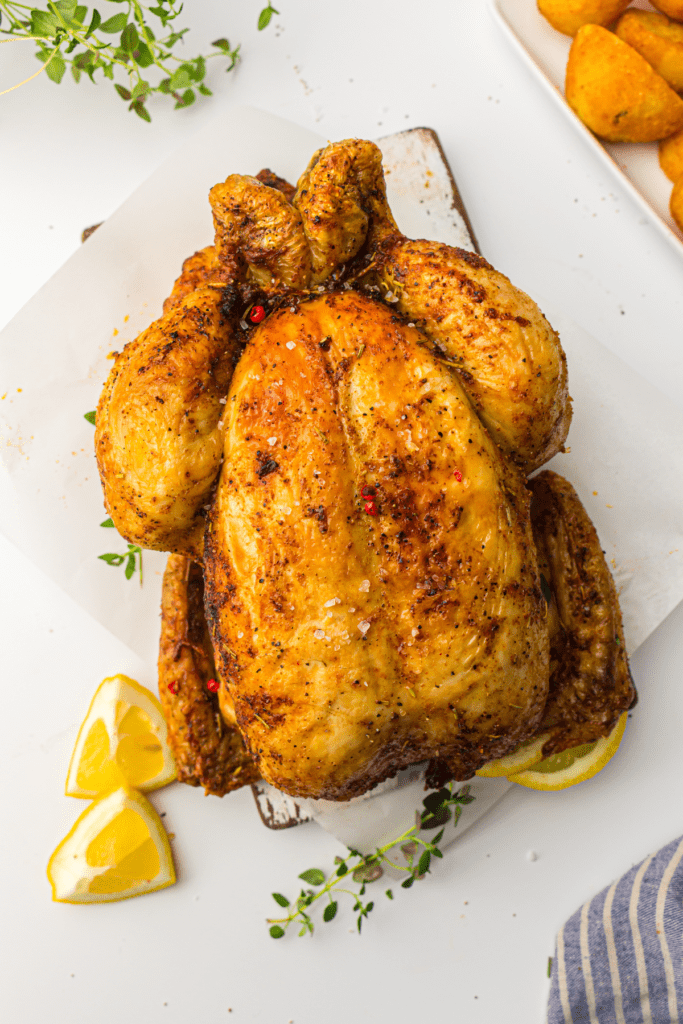 Air Fryer whole chicken with crispy skin garnished with lemon slices and fresh herbs on a white platter.