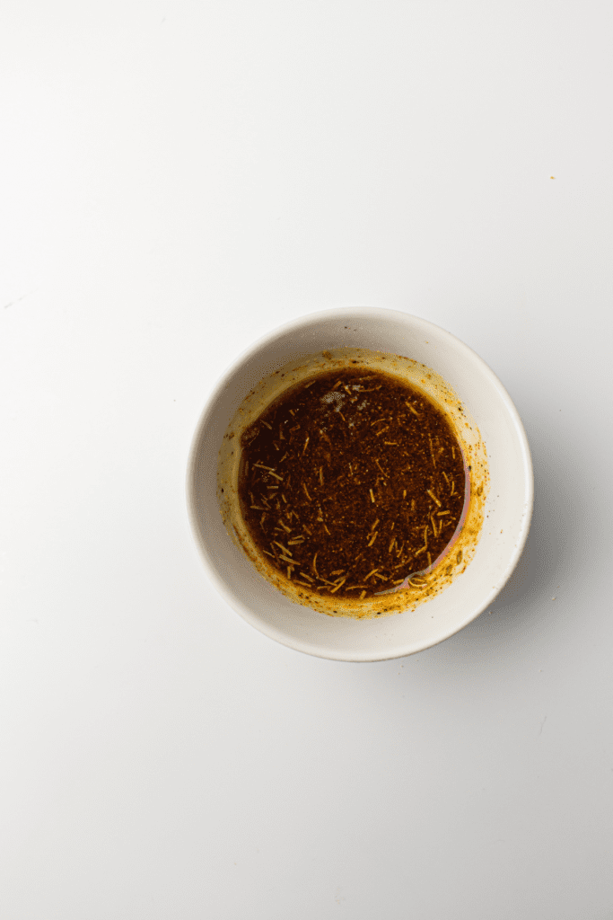 A white bowl containing a mix of red chili powder, green dried herbs and avocado oil.