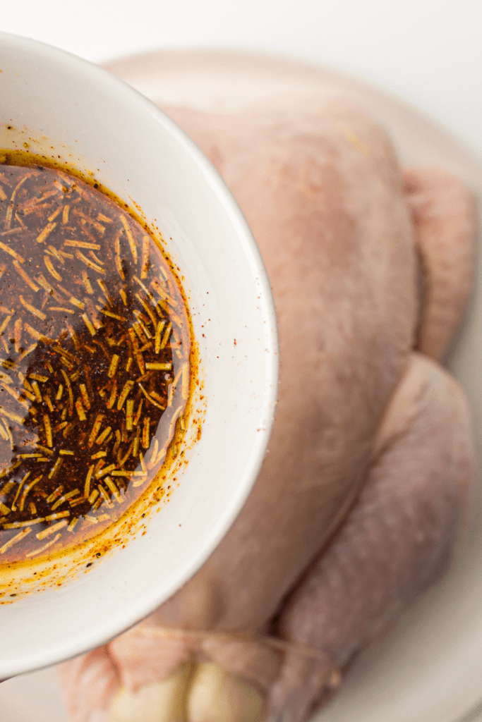 white bowl with seasoning and oil about to be poured onto a whole chicken.