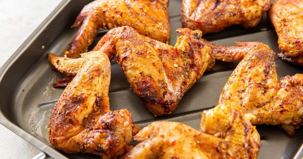 Baked chicken wings seasoned with spices on a black oven tray.