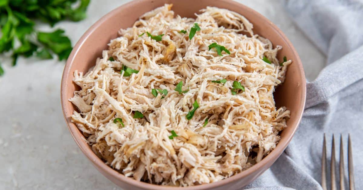 How to Make Air Fryer Shredded Chicken on a fork in a tan bowl with parsley.