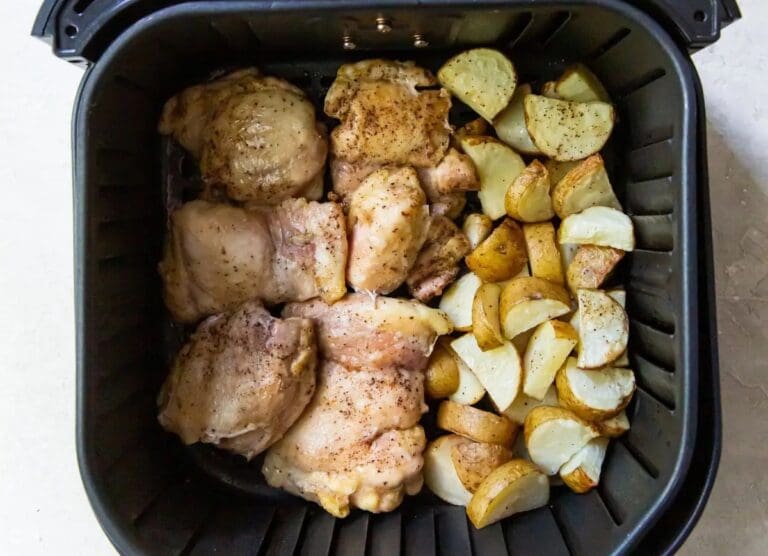 Chicken thighs and potato pieces placed inside an air fryer, seasoned and ready to be cooked—perfect for healthy cooking and delicious family meals.