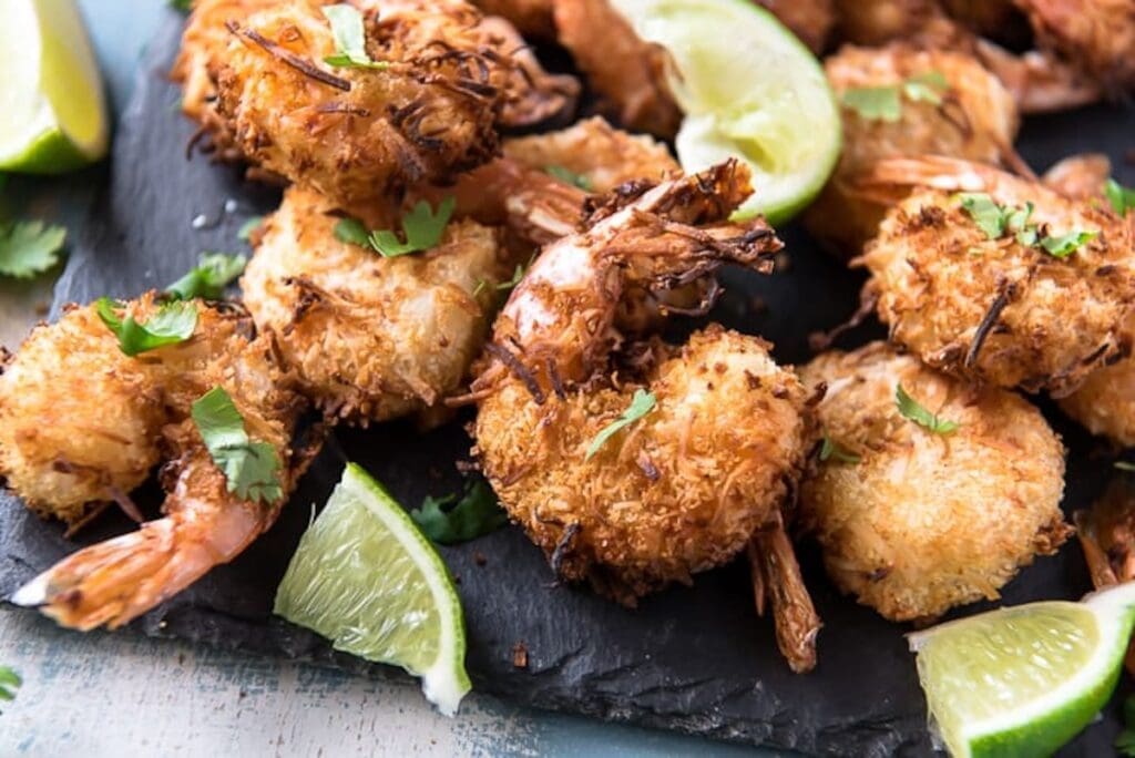 Coconut shrimp garnished with cilantro, served on a black slate with lime wedges. Perfect for lunch this week, this dish is both delicious and easy to make.