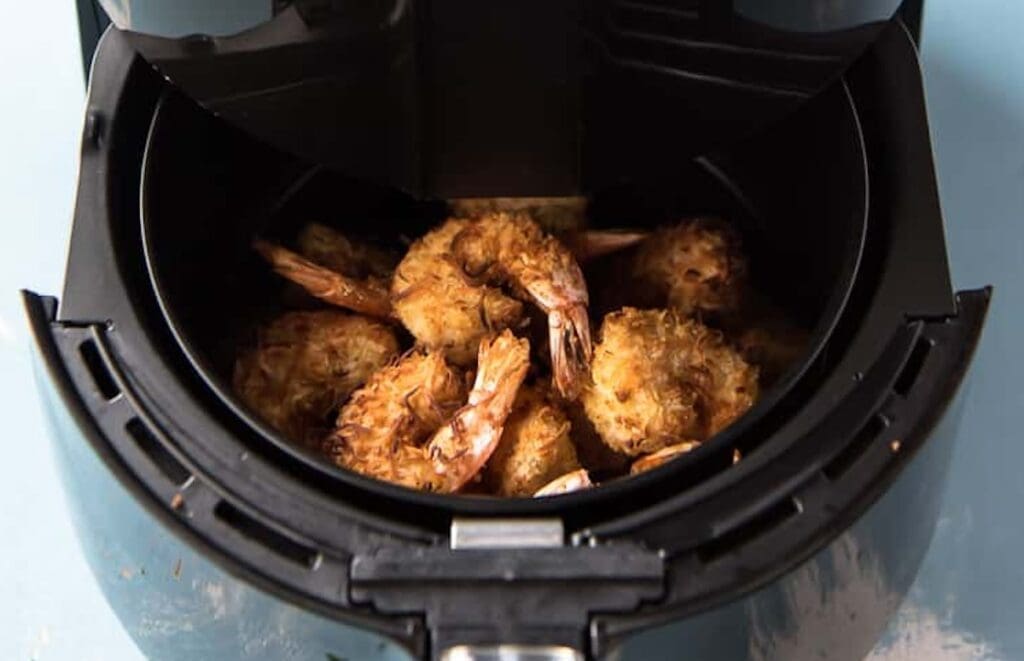 Close-up of cooked shrimp in an air fryer basket, perfect for lunch. The shrimp appear crispy and golden brown. The air fryer is open, showing the shrimp inside – a delightful addition to your go-to air fryer recipes this week.