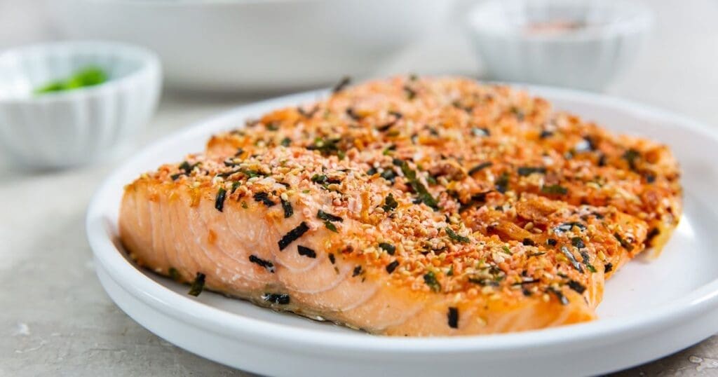 A plated dish featuring baked salmon fillet seasoned with herbs and spices on a white plate, perfect for lunch this week.