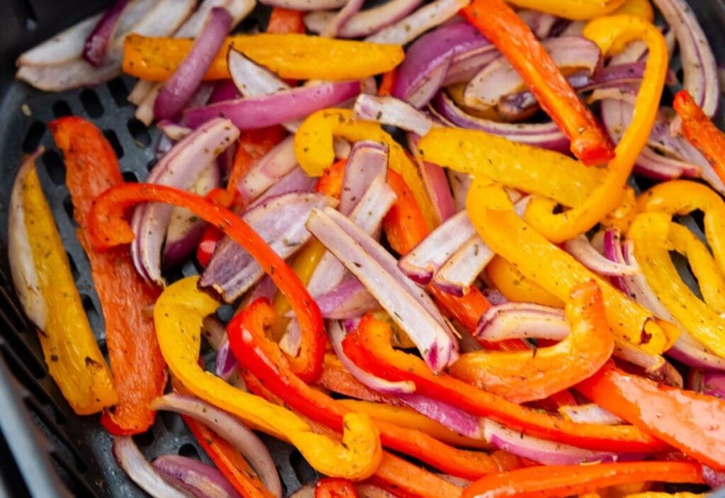 A close-up of sliced red onions, red bell peppers, and yellow bell peppers mixed together, seasoned and cooked in a pan. This mouthwatering side perfectly complements any main dish.