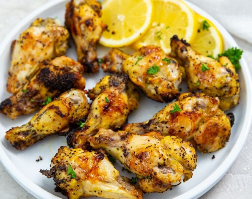 A plate of seasoned, roasted chicken drumsticks garnished with parsley and accompanied by lemon slices offers a delightful variety. Perfect for air fryer dinners, these succulent drumsticks ensure each day is filled with delicious flavor.