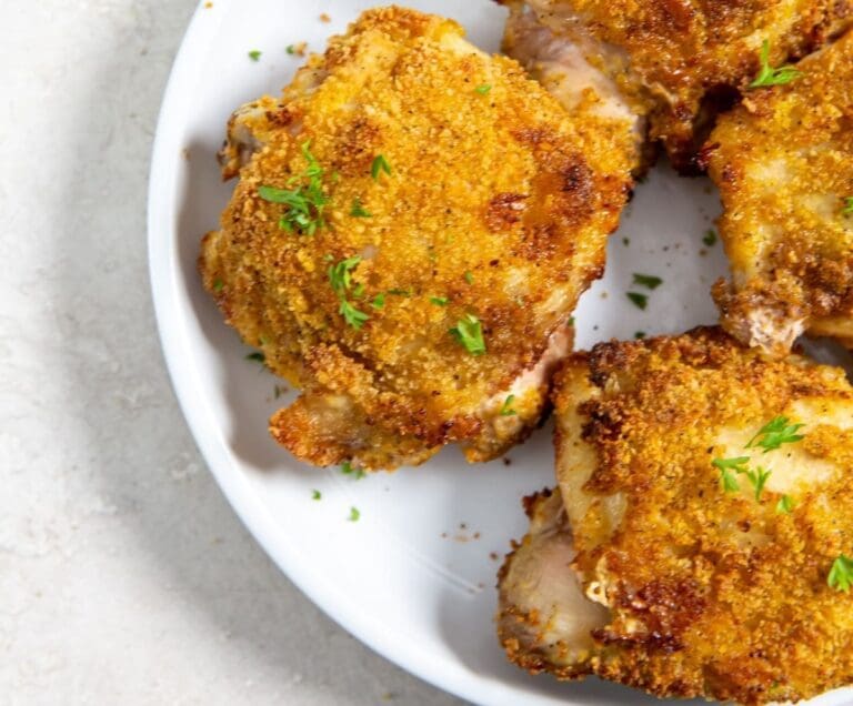 A white plate with crispy, air-fryer breaded chicken thighs, garnished with fresh herbs, on a light-colored surface.