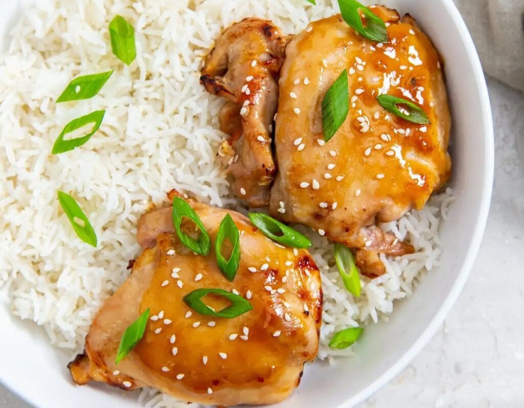 A quick bowl of white rice topped with two pieces of glazed chicken thighs, garnished with sesame seeds and sliced green onions. Ideal for air fryer recipes!