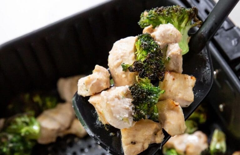 A spatula holding cooked chicken pieces and broccoli hovers above an air fryer basket, showcasing a quick and easy air fryer recipe to save time in the kitchen.