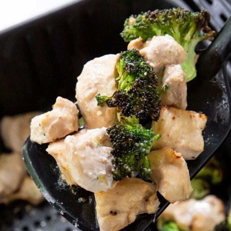 Chicken Air Fryer Recipes That'll Save You 30 Minutes Close Up of Chicken and Broccoli on a Spatula Hovering Above an Air Fryer Basket