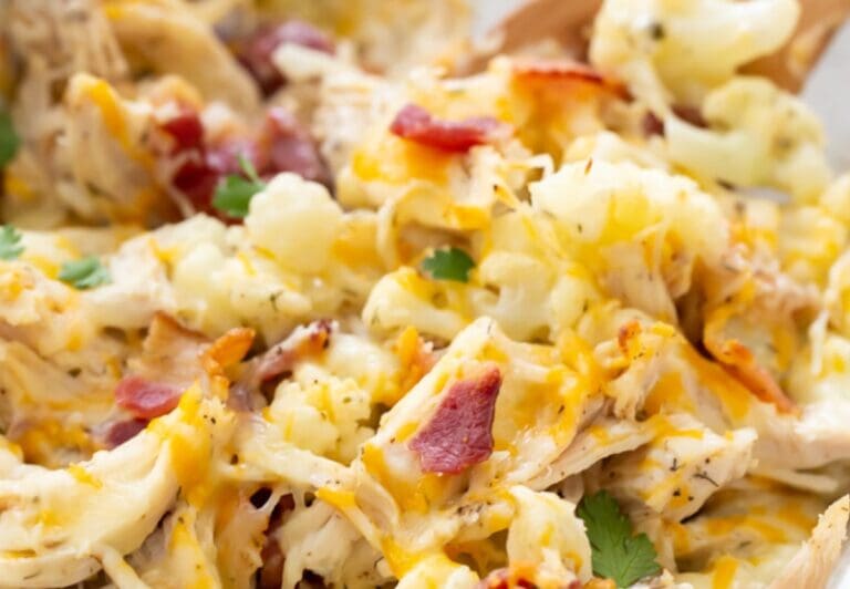 A close-up shot of a cheesy casserole featuring tender chicken and bacon, topped with herbs and melted cheese—a dish you need right now.