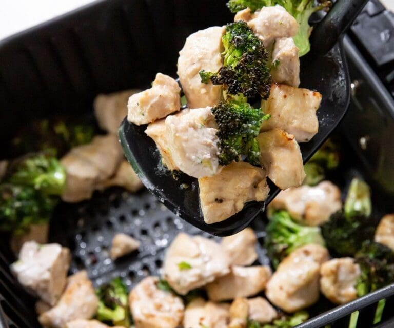 10 Air Fryer Recipes Close Up of Chicken and Broccoli Above an Air Fryer Basket on a Spatula