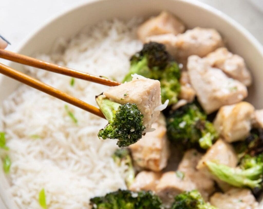 11 Easy Air Fryer Chicken Meals You Can Make Half Asleep Close Up of a Piece of Cooked Chicken Over a Bowl of Rice and Broccoli