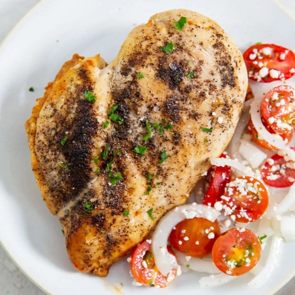 High Protein Chicken Recipes a Cooked Chicken Breast with Tomatoes and Onions on a White Plate