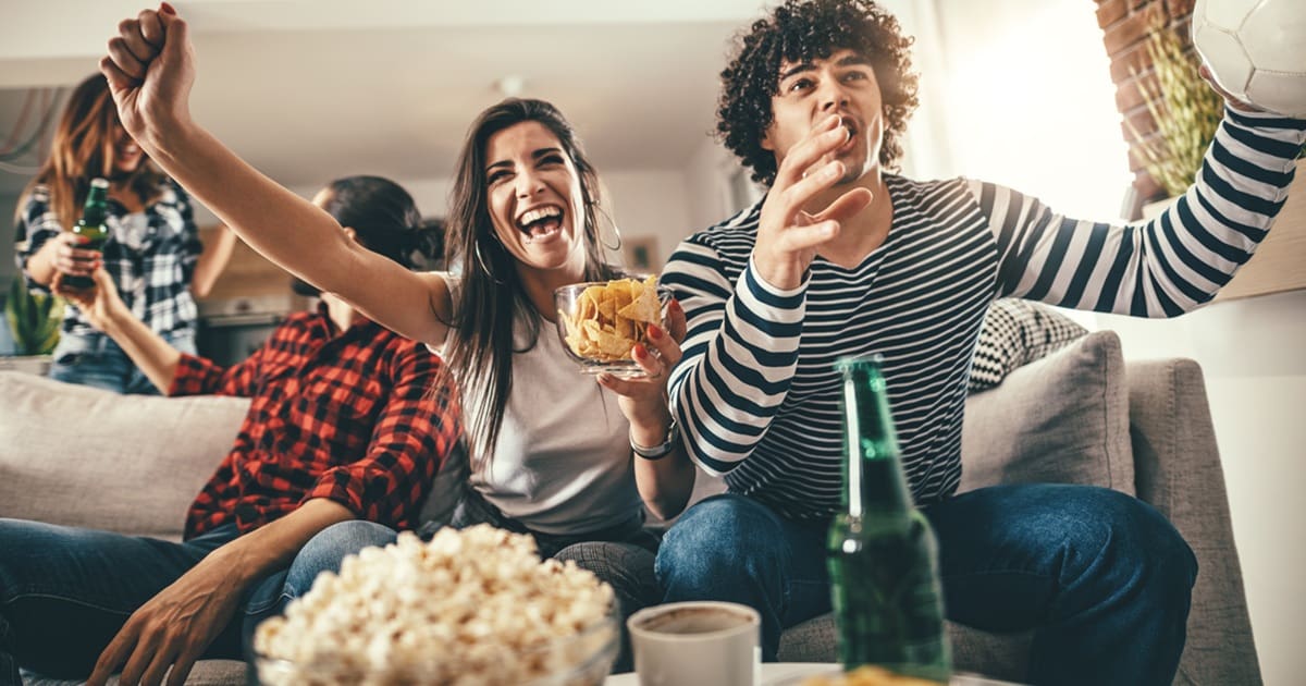 Super Bowl Air Fryer Recipes Two People Sitting on a Couch Watching Sports on TV and Cheering