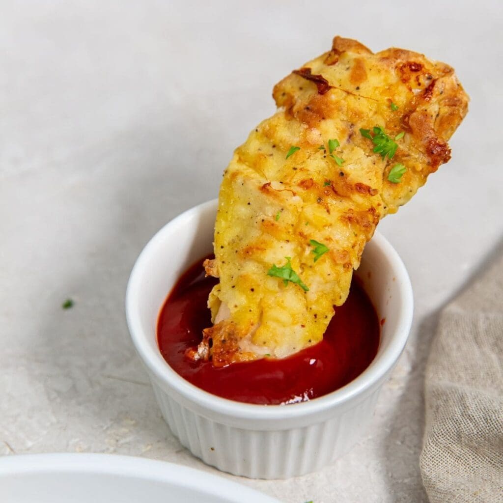 St. Patricks Day Air Fryer Recipes Close Up of a Chicken Tender Dipped into a Small Ramekin of Ketchup