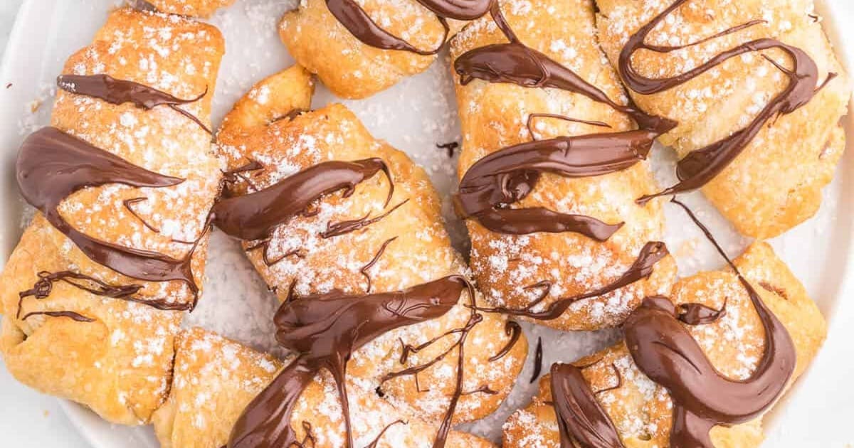Air Fryer Croissants on a Plate Drizzled with Chocolate and Sprinkled with Powder Sugar