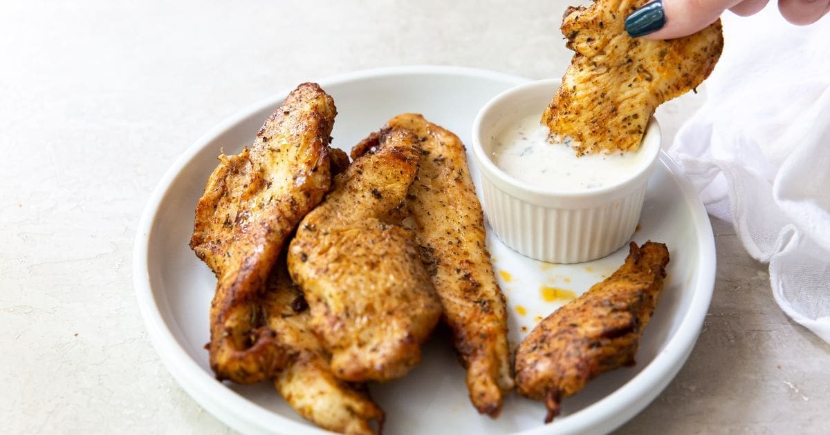 30 Flavorful Chicken Air Fryer Recipes That Prove 'Em Wrong a Plate of Air Fryer Chicken Breast Strips with One Being Dipped into Ranch Dressing