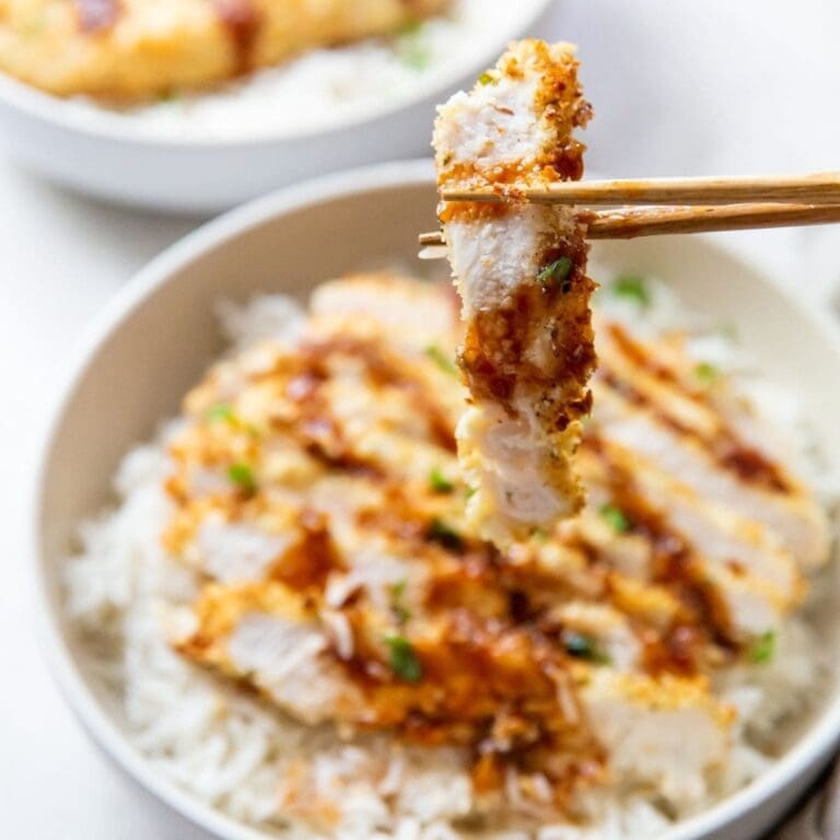 Quick and Easy Dinner a Piece of Katsu Chicken Being Held by Chopsticks Hovering Above a Bowl of Rice Topped with Katsu Chicken