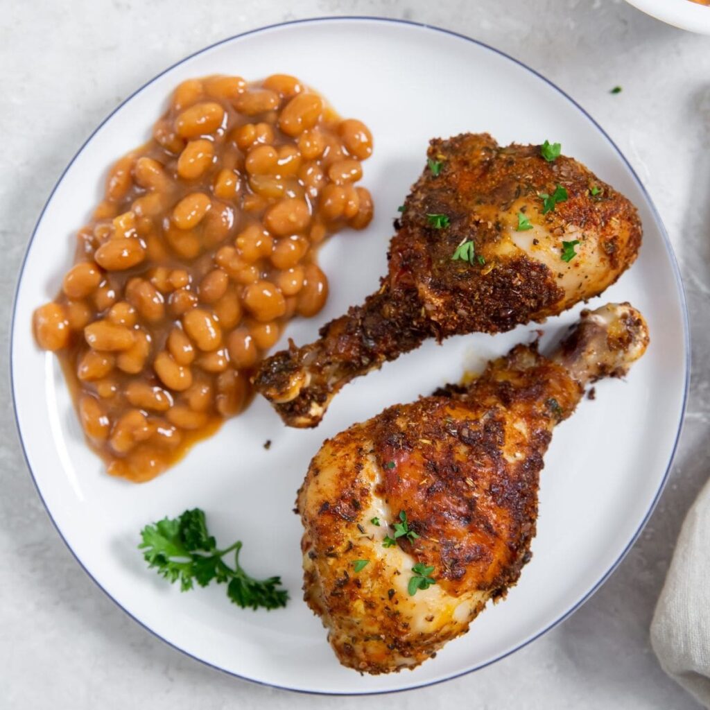 30-Minute Chicken Air Fryer Recipes a White Plate with Baked Beans and Two Drumsticks on it