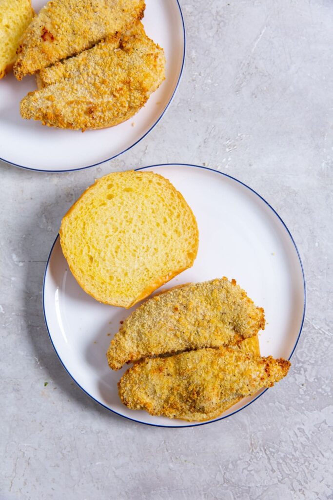 Air Fryer Katsu Chicken Sandwich Two Plates Each with Burger Buns Opened and Breaded Chicken Strips on the Bottom Buns