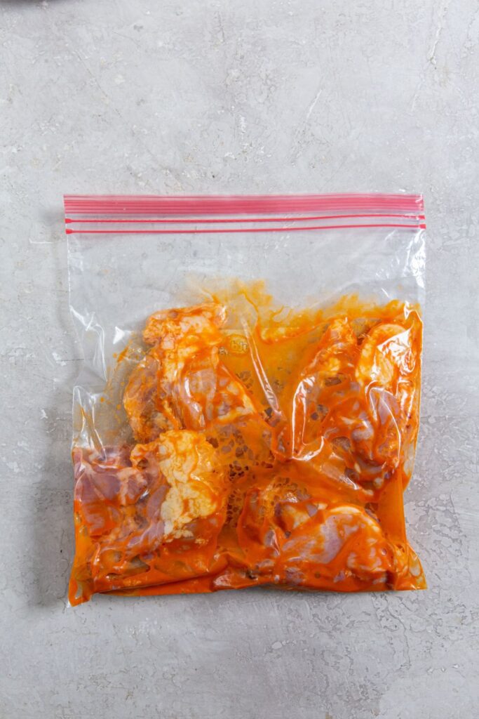 Air Fryer Buffalo Chicken Thighs ziplock bag with chicken covered in buffalo sauce inside