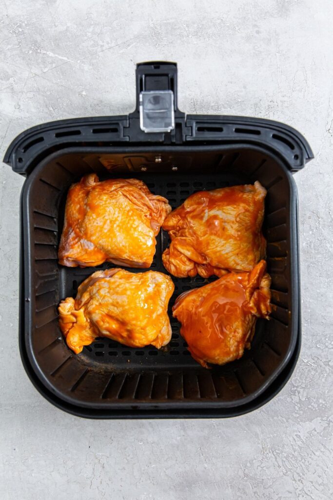 Air Fryer Buffalo Chicken Thighs black air fryer basket with raw chicken inside