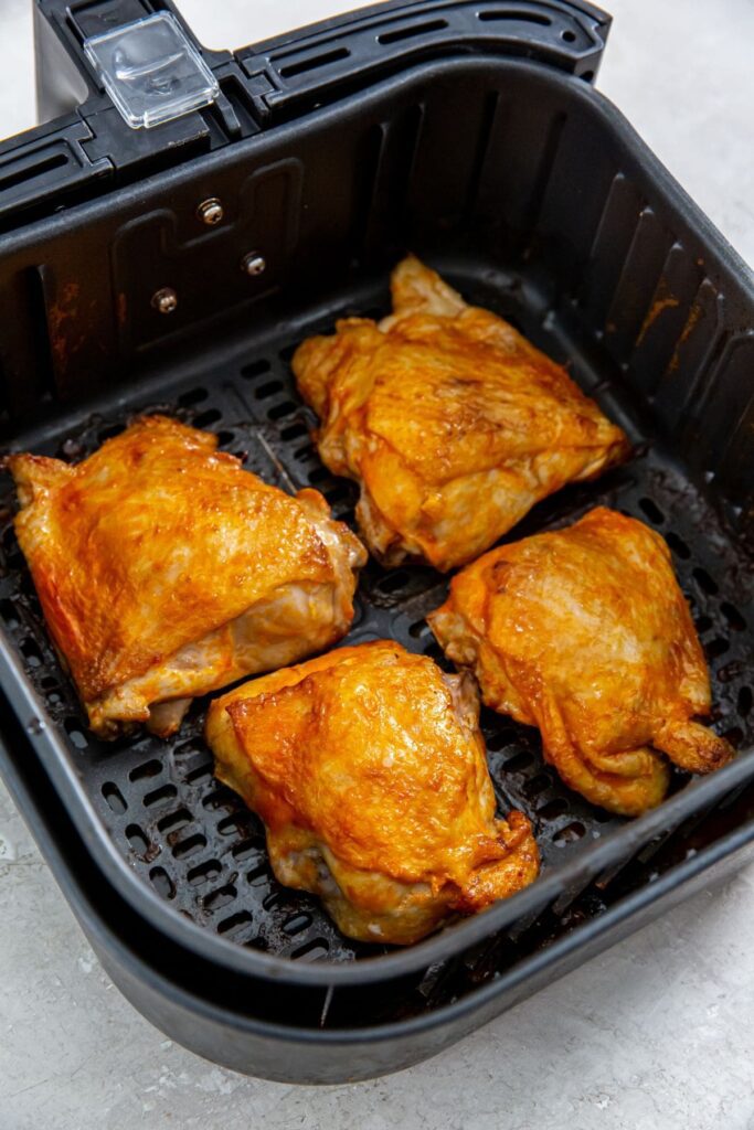 Air Fryer Buffalo Chicken Thighs black air fryer basket with cooked chicken inside