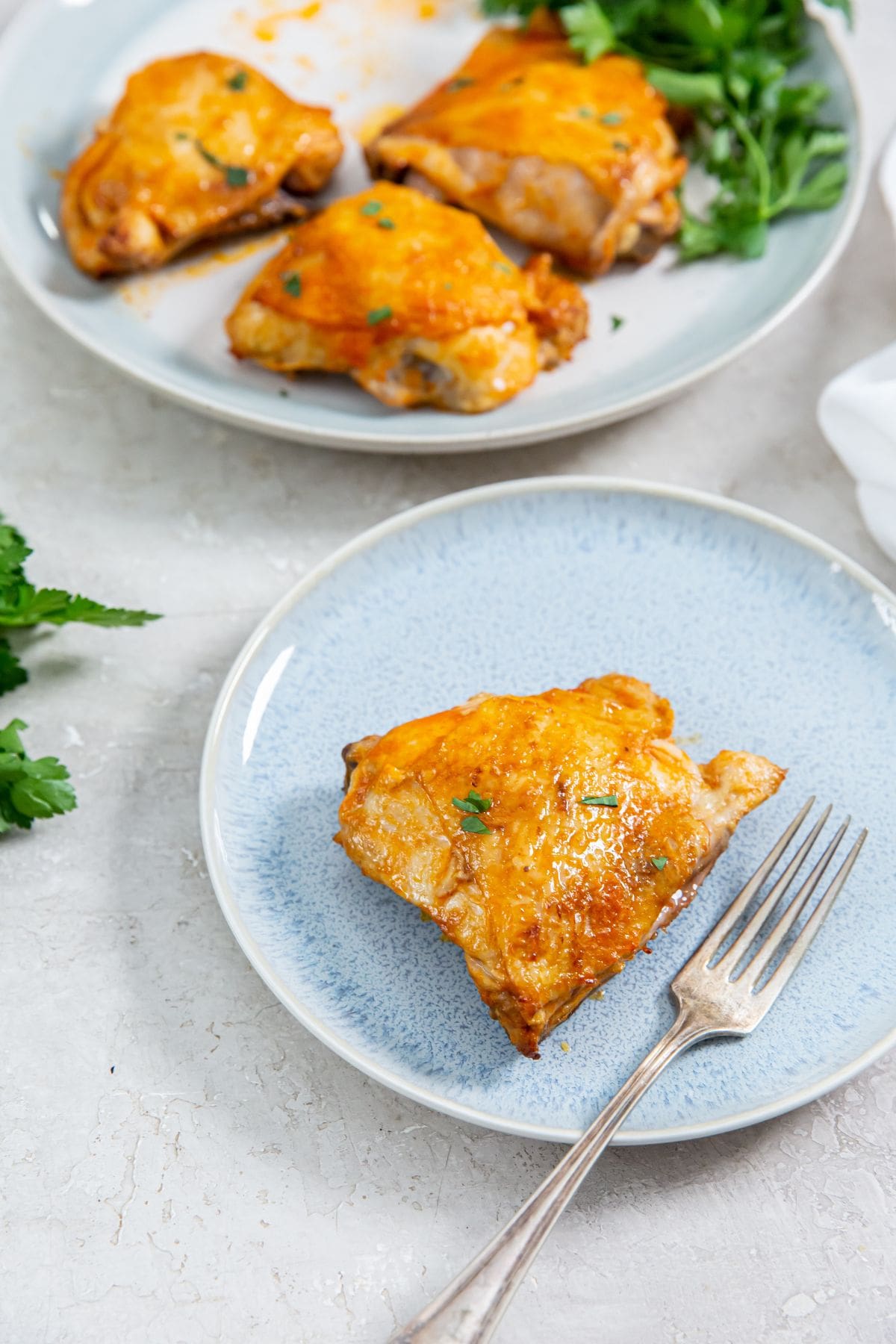 Air Fryer Buffalo Chicken Thighs blue plate with chicken and fork on. parsley and another plate in the background.