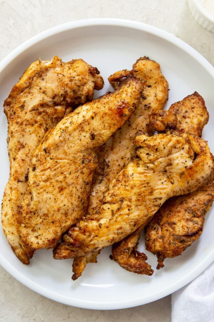 Air Fryer Chicken Breast Strips White plate full of cooked chicken breast strips