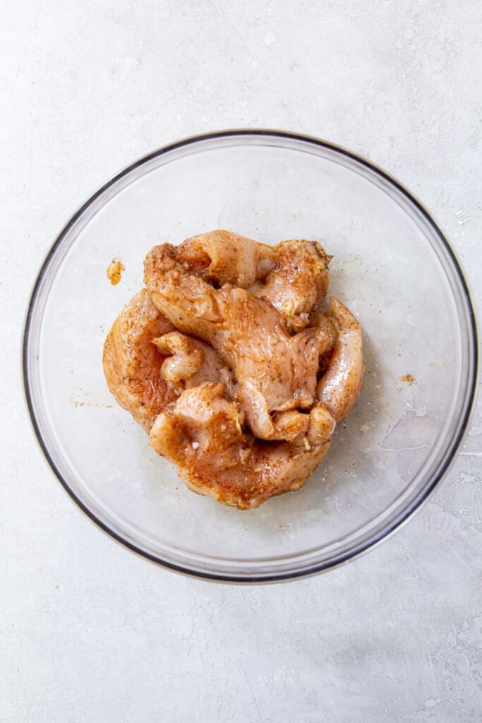 Air Fryer Chicken Breast Strips Gray background with clear bowl chicken tossed in the ingredients