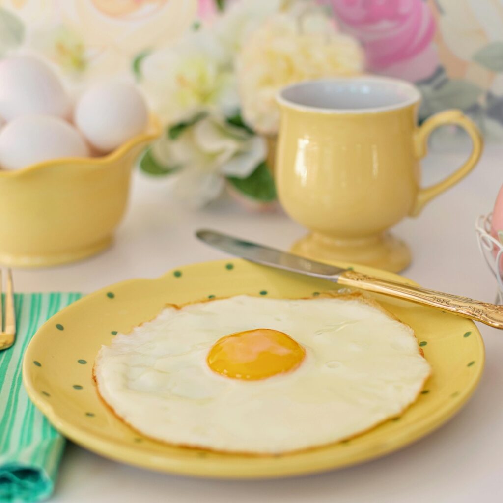 Air Fryer Easter Brunch Recipes Sunny Side Up Egg on a Yellow Plate Next to a Yellow Mug, with Flowers in the Background on a Table