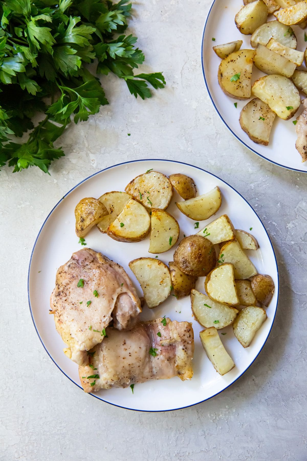 Air Fryer Chicken Thighs and Potatoes plate with chicken thighs and potatoes on it. parsley and another plate in the background