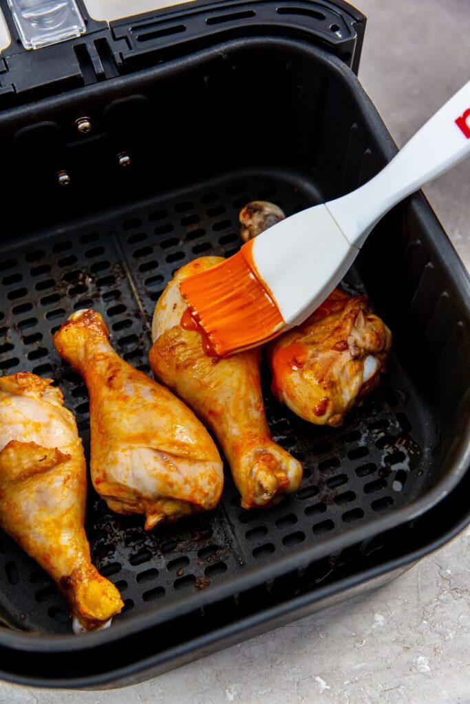 Air Fryer Buffalo Chicken Legs black air fryer basket with chicken inside being brushed with sauce
