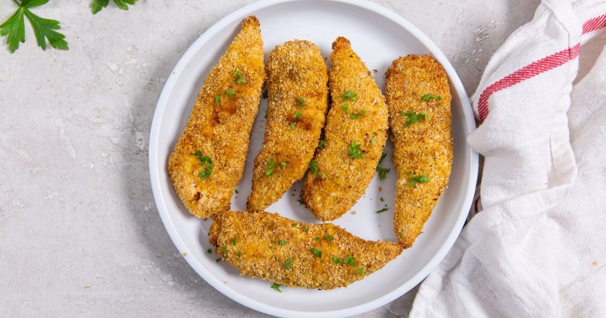 Air Fryer Shake N Bake Chicken Tenders plate with chicken tenders. parsley sprinkled on top and in the back