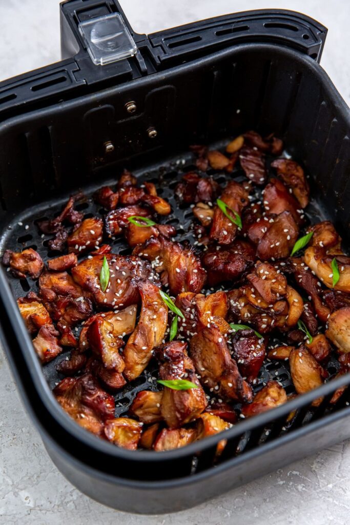 Air Fryer Trader Joe&rsquo;s BBQ Teriyaki Chicken black air fryer basket with cooked chicken inside. tossed in sauce scallions and sesame seeds
