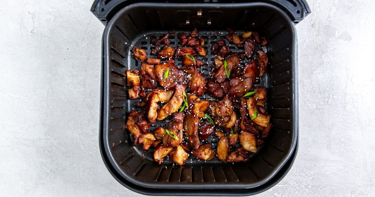 Air Fryer Trader Joe&rsquo;s BBQ Teriyaki Chicken two bowls with chicken and rice inside them. gray towel in the back along with chopsticks and sesame seeds