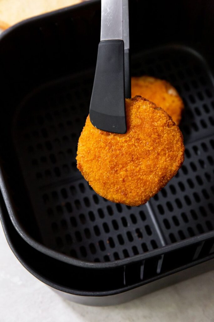 Air Fryer Chicken Patty holding a chicken patter over the air fryer basket