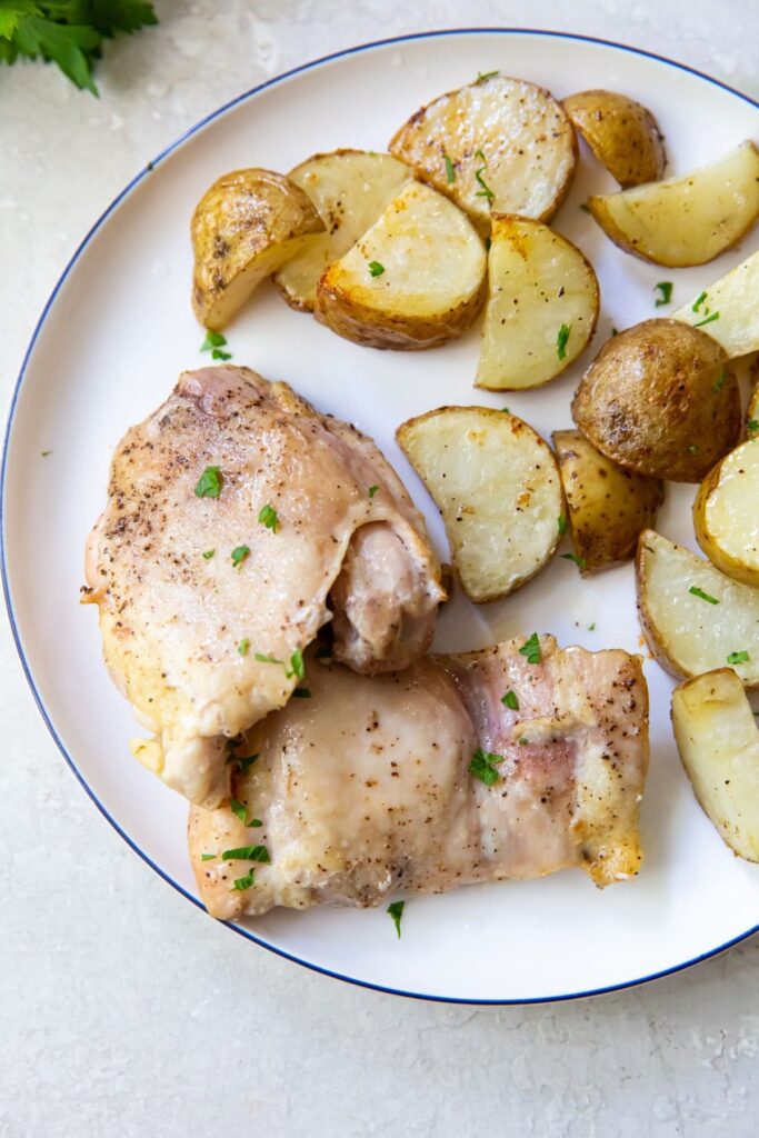 Air Fryer Chicken Thighs and Potatoes plate with chicken thighs and potatoes on it. parsley in the background