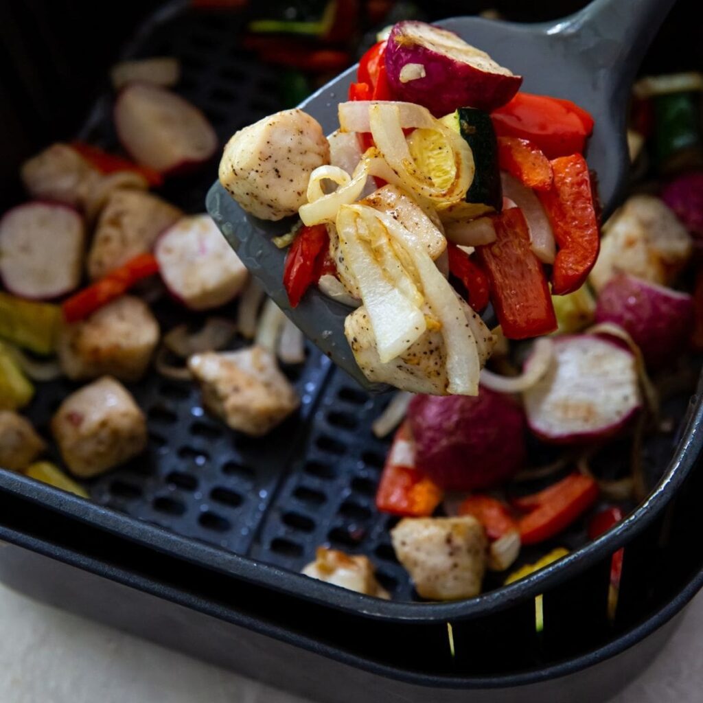 Healthy Air Fryer Meals with Chicken a Spatula Hovering Above an Air Fryer Basket Filled with Chicken and Veggies