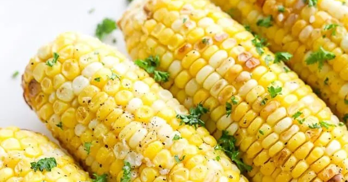 Patriotic Memorial Day Air Fryer Recipes Close Up of Four Air Fryer Corn on the Cob Garnished with Green Herbs and Butter