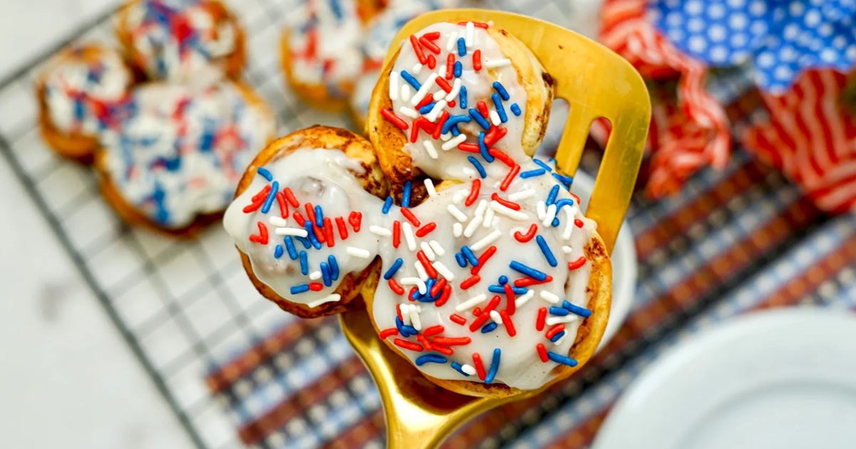 Patriotic Memorial Day Air Fryer Recipes Close Up of a Patriotic Mickey Cinnamon Roll on a Golden Spatula Above a Cooling Rack of Patriotic Mickey Cinnamon Rolls